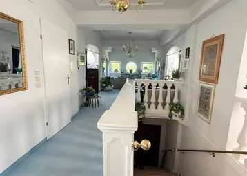 Langer Flur mit Treppenabgang, blauer Auslegware und Blick in den Wohnbereich.