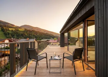 Geräumiger Balkon mit Holzboden, Sitzgelegenheiten und malerischem Bergblick bei Sonnenuntergang.