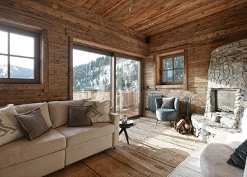 Gemütliches Wohnzimmer im alpinen Stil mit Holzwänden, Steinkamin und Panoramablick auf die verschneiten Berge.