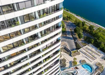 Moderne Wohnanlage mit geschwungener Architektur, Balkonen und einem Poolbereich am Wasser.