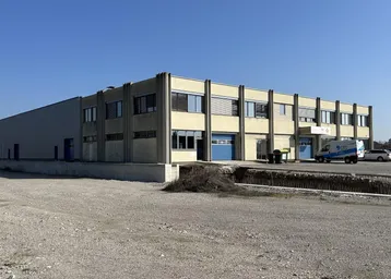 Großes Industriegebäude mit Büroflächen und Lagerhallen auf einem weitläufigen Gelände unter blauem Himmel.