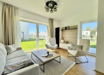 Helles Wohnzimmer mit großen Fenstern, die einen Blick auf den Garten und die moderne Siedlung bieten.