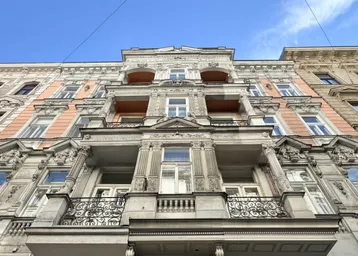 Prächtige Altbaufassade mit reich verzierten Balkonen und architektonischen Details unter blauem Himmel.