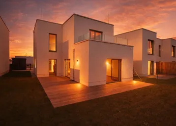 Modernes Einfamilienhaus mit Holzterrasse und Balkon, beleuchtet vom warmen Licht des Sonnenuntergangs.