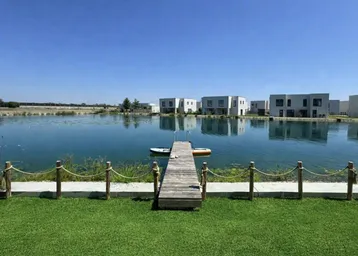 Blick über den gepflegten Rasen und den Steg auf den See mit modernen Häusern am Ufer.