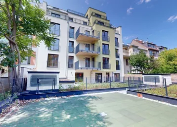Modernes Mehrfamilienhaus mit Balkonen und einer kleinen Grünfläche im Vordergrund unter blauem Himmel.