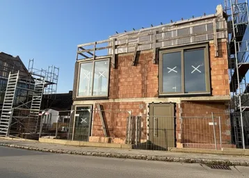 Neubau im Rohbauzustand mit großen Fenstern, Gerüst und massiver Bauweise.