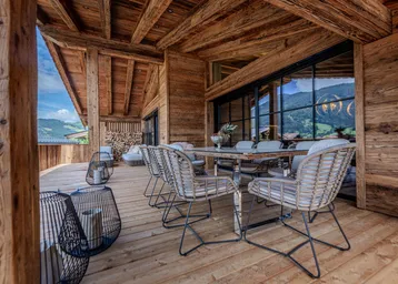 Geräumige überdachte Terrasse mit Holzboden, Esstisch und Bergblick, ideal für Mahlzeiten im Freien.