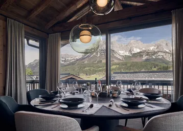 Elegantes Esszimmer mit Holzakzenten, großem Esstisch und atemberaubendem Bergblick durch Panoramafenster.