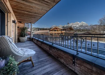 Geräumiger Balkon mit Holzboden, gemütlichem Sessel und beeindruckendem Bergblick in sonniger Lage.