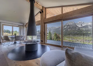 Geräumiger Wohn-Essbereich mit modernem Kamin, Holzbalken und Panoramafenstern mit Bergblick.