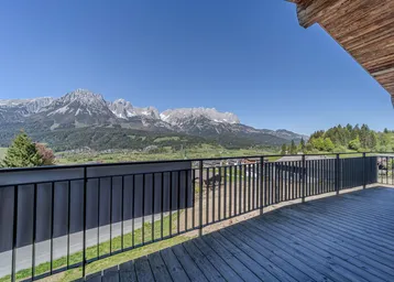 Geräumiger Holzbalkon mit Metallgeländer und weitem Blick auf die umliegende Berglandschaft.