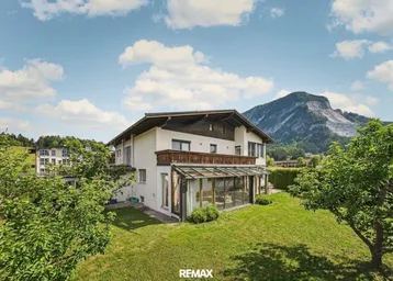 Freistehendes Haus mit Wintergarten, großem Garten und beeindruckendem Bergblick unter blauem Himmel.