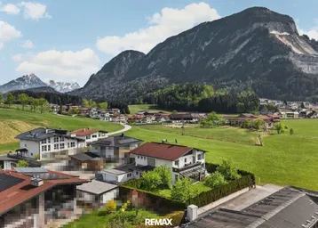 Panoramablick auf ein malerisches Dorf in einer grünen Berglandschaft mit vielen Häusern und Dächern.