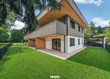 Modernes Wohnhaus mit Holzfassade, großem Garten und gepflasterter Terrasse im Grünen.