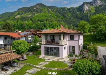 Charmantes Haus mit Steinfassade und Ziegeldach, umgeben von grüner Natur und Bergen.