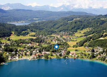 Panoramablick aus der Vogelperspektive auf ein Dorf am See mit umliegenden Bergen und Wäldern.