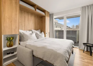 Helles Schlafzimmer mit integriertem Schrankbett, Holzelementen und Zugang zum Balkon.