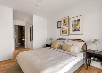 Helles Schlafzimmer mit Holzboden, modernem Bett und Zugang zu einem Ankleidebereich mit Bad.