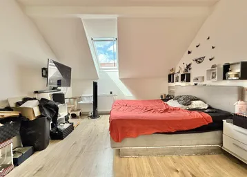 Helles Schlafzimmer im Dachgeschoss mit Dachfenster, Holzboden und schrägen Wänden.