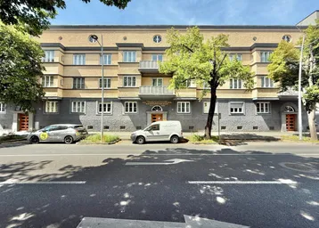 Ansicht der Wohnhausfassade von der Straße aus mit geparkten Autos und Bäumen.
