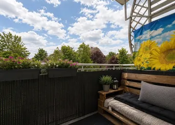 Gemütlicher Balkon mit Sitzgelegenheiten aus Paletten und Blumenkästen.