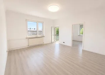 Heller, leerer Raum mit Laminatboden, Fenster und Zugang zu einem Balkon.