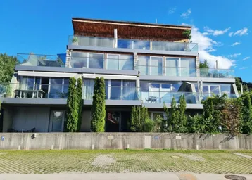 Moderne Terrassenwohnungen mit Glasbalkonen und großen Fensterfronten unter blauem Himmel.