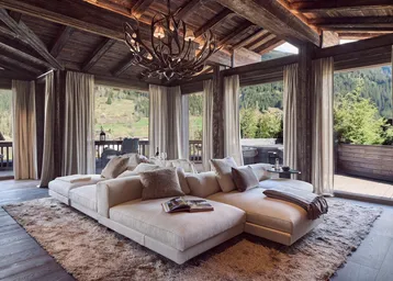 Luxuriöses Wohnzimmer mit Holzbalkendecke, großem Sofa und Panoramafenstern mit Bergblick.