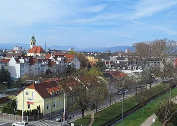 Weitläufiger Stadtblick mit historischen Gebäuden und Bergen im Hintergrund.