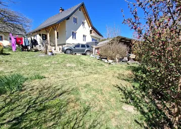 Haus mit großem, grünem Garten auf einem Hanggrundstück unter blauem Himmel.