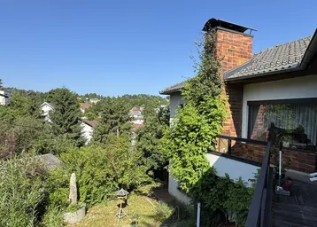 Balkon mit Blick ins Grüne und auf die umliegende Wohngegend unter blauem Himmel.