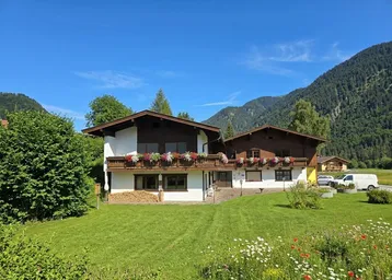 Traditionelles Haus im Alpenstil mit Holzbalkonen und gepflegtem Garten vor Bergkulisse.