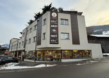 Modernes Geschäftsgebäude mit mehreren Etagen und großen Schaufenstern, umgeben von Schnee und Bergen.