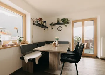 Heller Essbereich mit Eckbank, Holztisch und Zugang zum Balkon, umgeben von Pflanzen.