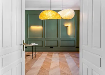 Helles Zimmer mit grünen Wandpaneelen, Fischgrätparkett und modernen Leuchten.