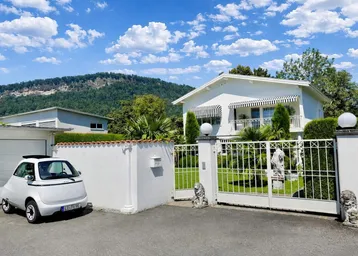 Eingangsbereich des Hauses mit schmiedeeisernem Tor, Garage und Bergkulisse im Hintergrund.