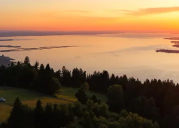 Atemberaubender Sonnenuntergang über einem weiten See, umgeben von bewaldeten Hügeln und einer weiten Landschaft.
