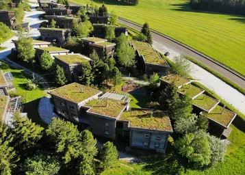 Luftaufnahme einer Siedlung mit Holzhäusern und begrünten Dächern in ländlicher Umgebung.