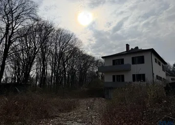 Hausfassade mit umliegender Natur und kahlen Bäumen unter bewölktem Himmel.
