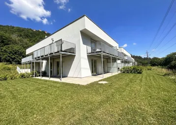 Moderne Wohnanlage mit weißer Fassade, Balkonen und direktem Zugang zu privaten Gärten.