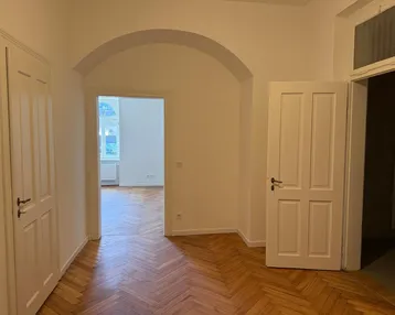Heller Flur mit Fischgrätparkettboden und weißen Türen, der zu weiteren Räumen führt.