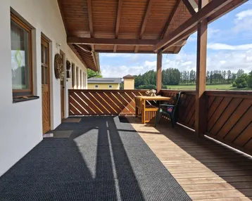 Überdachter Balkon mit Holzboden und Sitzgelegenheiten, bietet einen weiten Blick auf die grüne Landschaft.