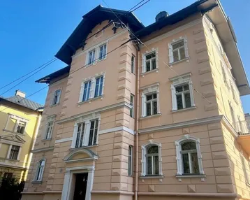 Historisches Gebäude mit eleganter Fassade und traditionellen Fenstern unter blauem Himmel.
