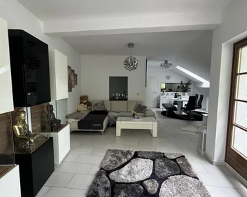 Helles, offenes Wohnzimmer mit modernen Möbeln, Fliesenboden und Blick in den Essbereich.