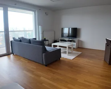 Heller Wohn- und Essbereich mit Parkettboden, großem Fenster und Zugang zum Balkon.