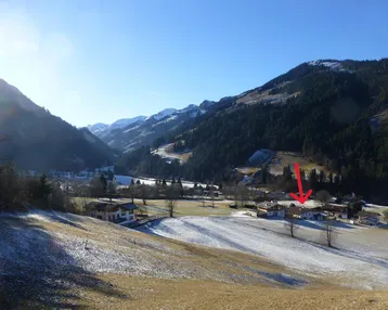 Weitläufige Ansicht eines verschneiten Tals mit Bergen und vereinzelten Häusern unter blauem Himmel.