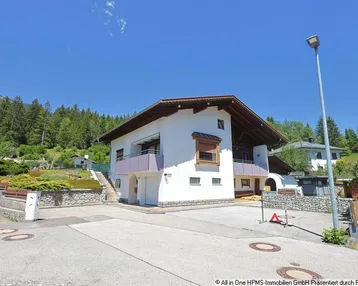 Freistehendes Haus mit weißer Fassade, Holzelementen und Balkonen in alpiner Umgebung.