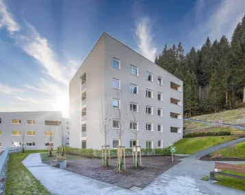 Moderne Wohngebäude in sonniger Hanglage mit gepflegten Außenanlagen und Wegen.