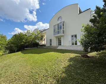 Modernes Gebäude mit geschwungener Architektur und großem Gartenbereich unter blauem Himmel.